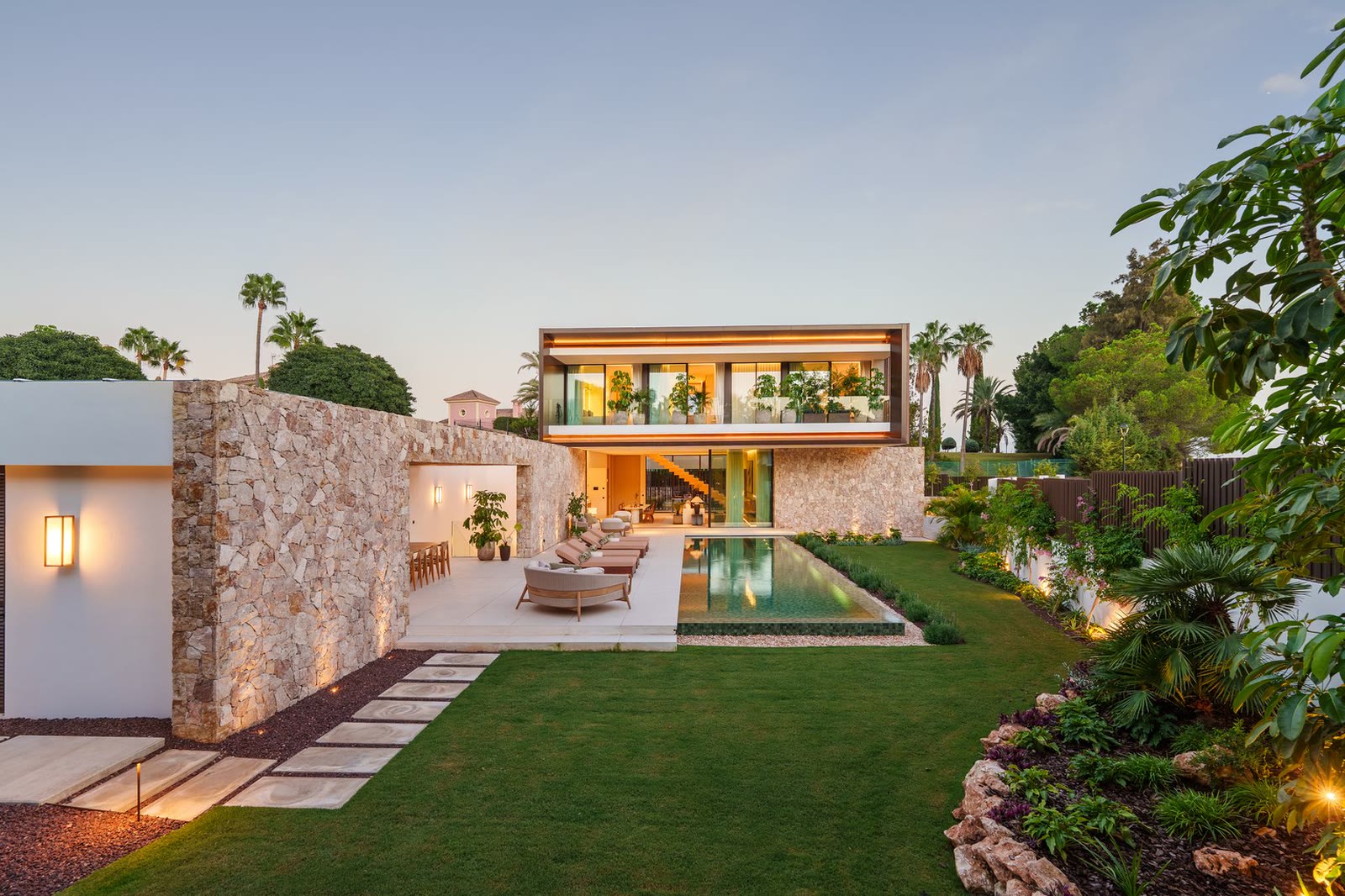 Listing photo: villa with natural stone wall, garden and pool in the evening